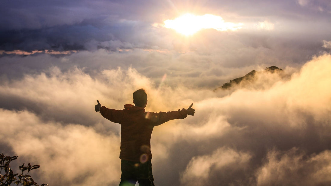 A man on top of the mountains facing the clouds and rising sun on golden hour.