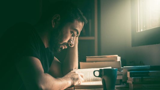 man reading a book at a desk with coffee mug on his side