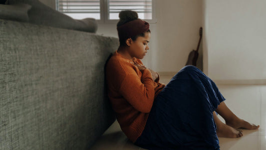 An anxious girl sitting on the floor with her hand on her chest.