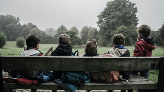 Five children sitting on a bench in front of trees.